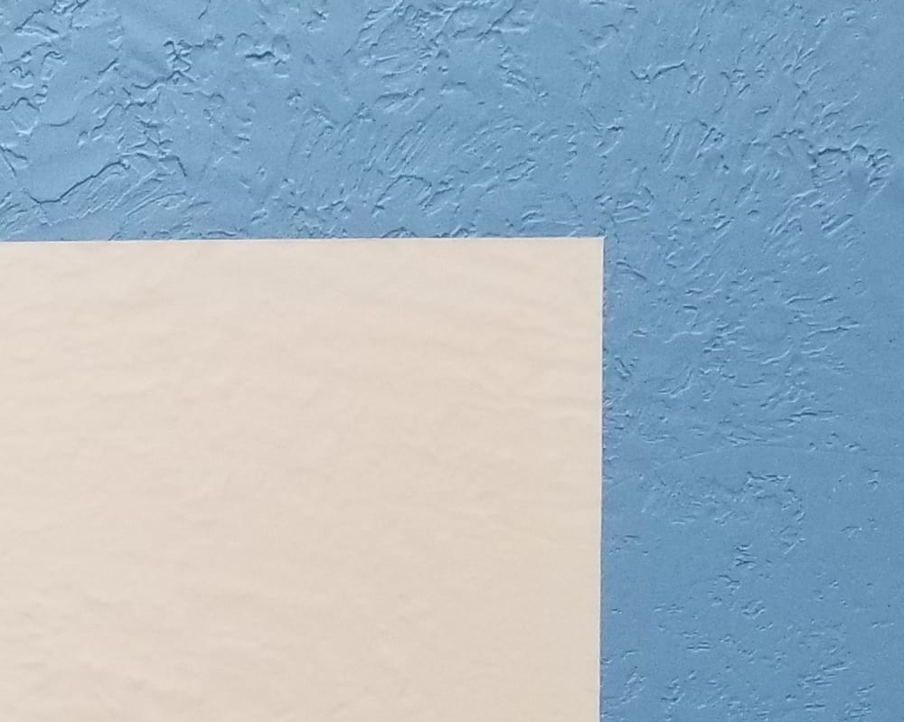 White wallpaper liner over blue knockdown texture.