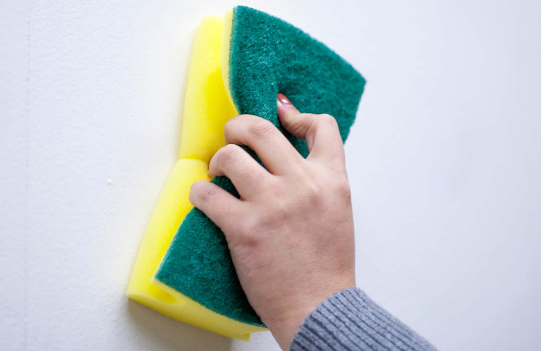 A hand wiping down a wall with a sponge.