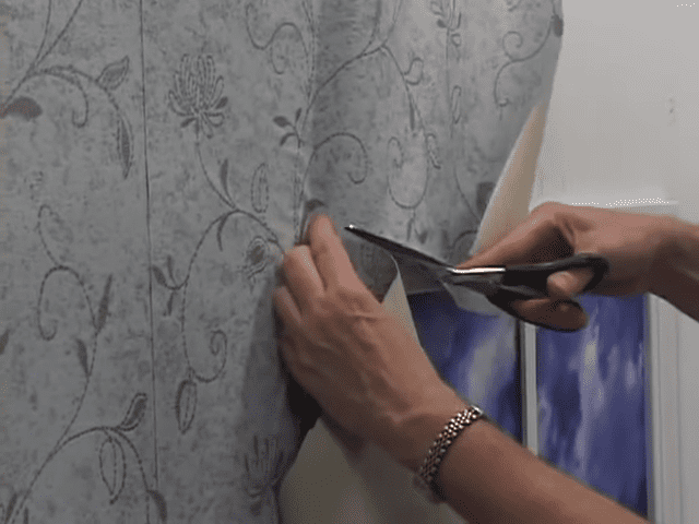 Scissors creating a relief cut in wallpaper around a window.