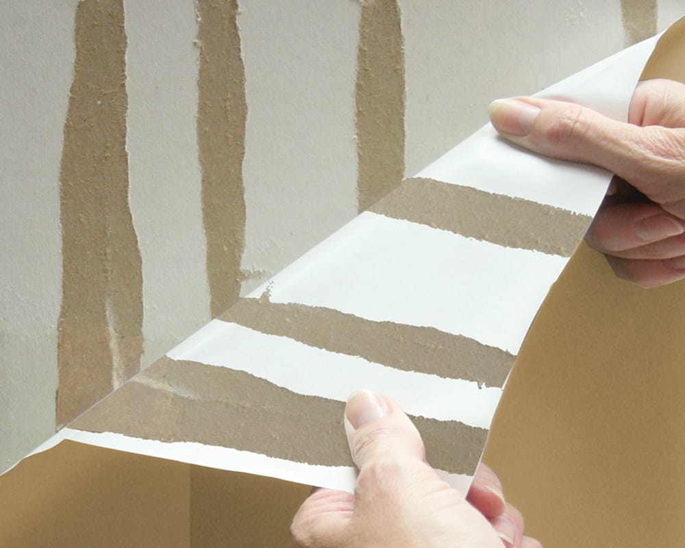 Close up of hands holding torn, damaged drywall paper.