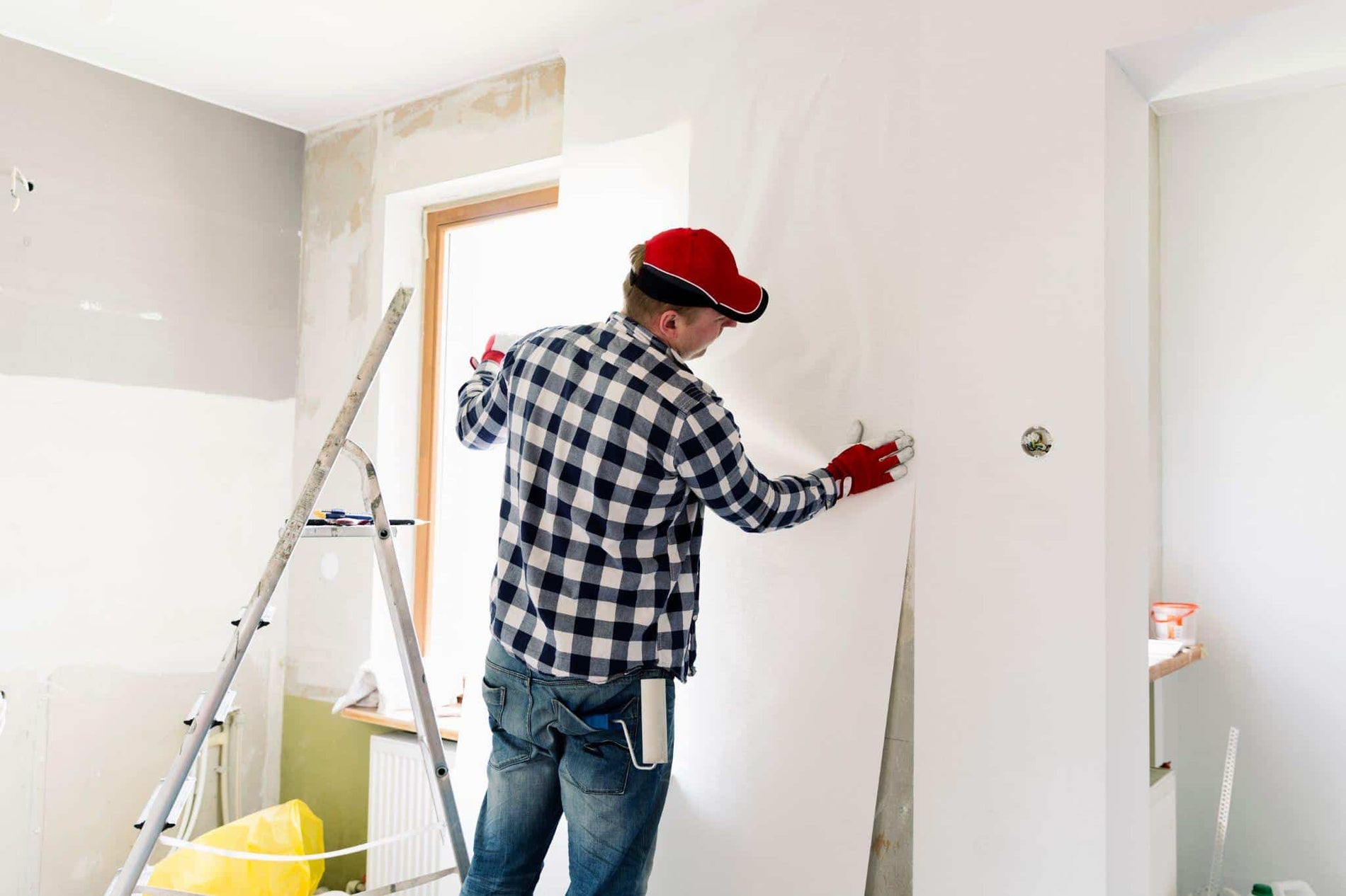 Young man, worker is putting up wallpapers on the wall.