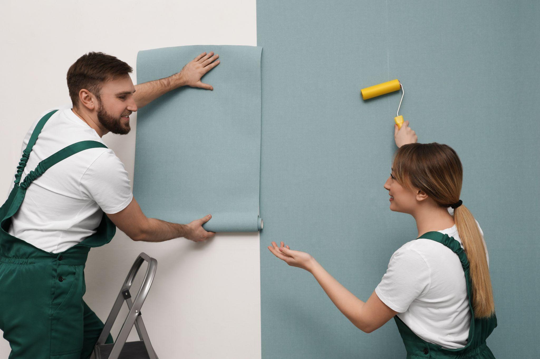 Workers hanging stylish wall paper sheet on wall