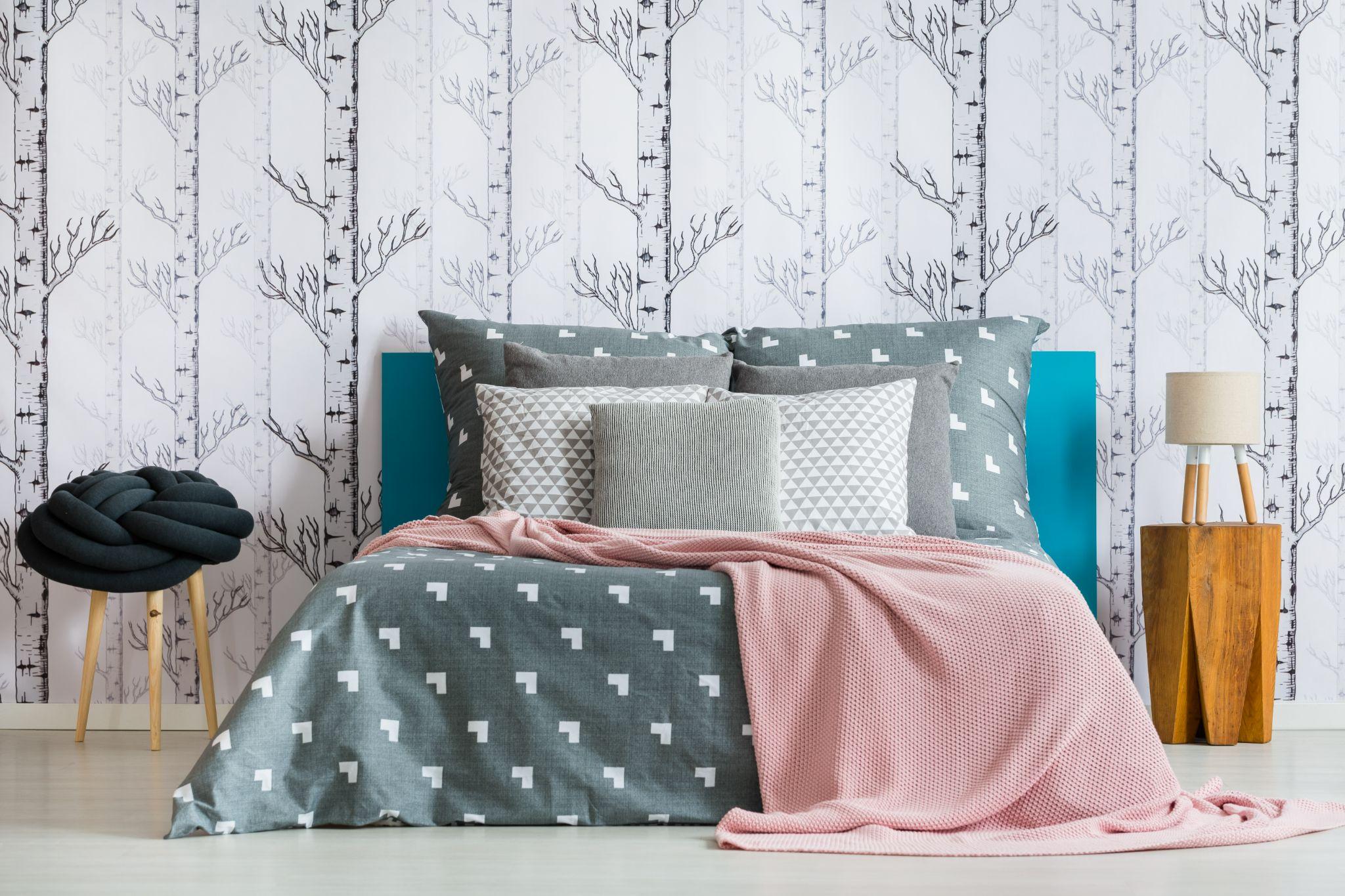 Pink blanket and knot pillow on king-size bed in bedroom with lamp on wooden stool