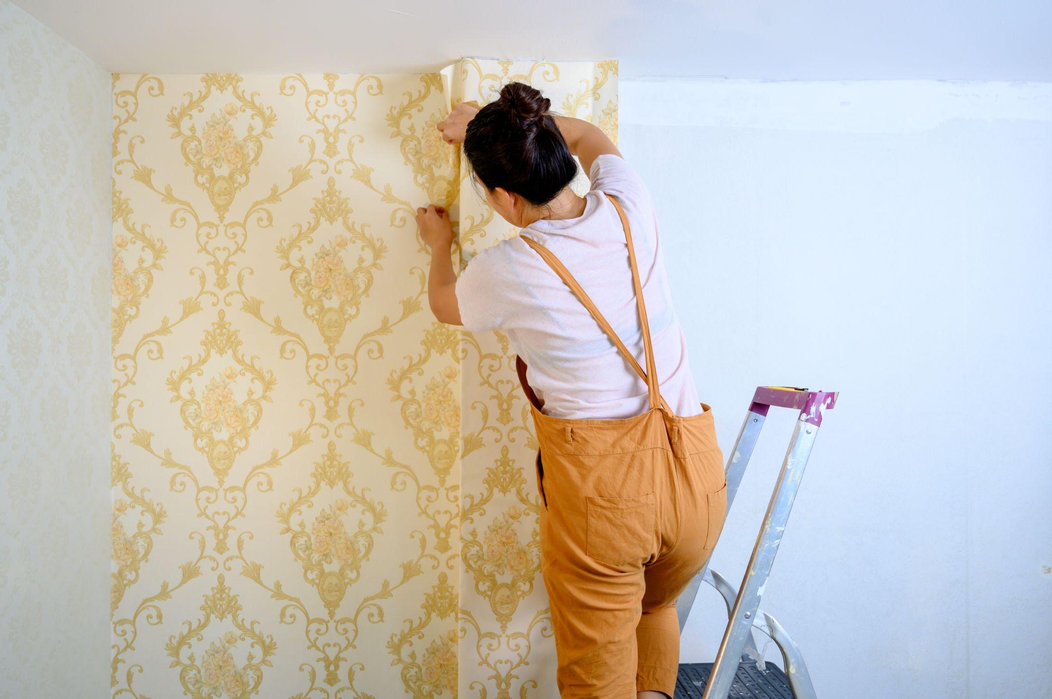 woman applying new wallpaper at home. Renovate and house decoration.